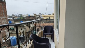 A balcony with a black plastic chair, a small table, and a blue water tank.