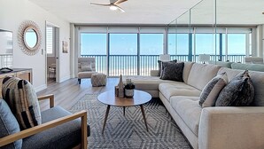 A spacious living room with a large sofa, a coffee table, and a ceiling fan. - Beachfront Getaway at Caper Beach Club #813 | Private Chiller/Heated Pool (Fort Myers Beach)