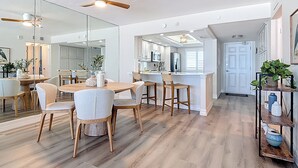 A modern kitchen with a central island, wooden flooring, and a dining area with a round table and chairs. - Beachfront Getaway at Caper Beach Club #813 | Private Chiller/Heated Pool (Fort Myers Beach)