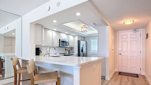 A modern kitchen with white cabinetry, a central island with bar stools, stainless steel appliances, and recessed lighting. - Beachfront Getaway at Caper Beach Club #813 | Private Chiller/Heated Pool (Fort Myers Beach)
