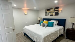 Un dormitorio con una cama, un mesita de noche, una lámpara de pared y un respiradero en el techo.