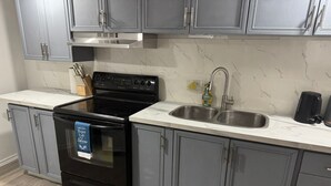 Una cocina con gabinetes grises, una estufa negra, un lavamanos de acero inoxidable y un salpicadero de mármol.