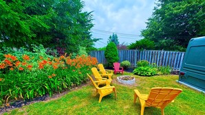 Un patio trasero con un brasero, sillas amarillas y una diversidad de plantas y flores.