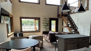 A spacious kitchen with a dining area, wooden flooring, and large windows providing natural light. - Hemlock Hideaway – Luxury Cabin - Romantic & Remote Getaway in Upstate, NY (Otego)
