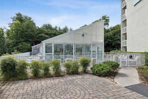 Un bâtiment moderne à la façade en verre, entouré d’une clôture blanche et de verdure.
