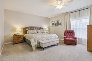 A bedroom with a bed, a chair, a nightstand, and a ceiling fan.