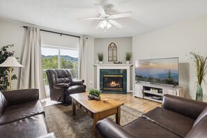 A living room with a fireplace, leather sofas, a television, and a ceiling fan.