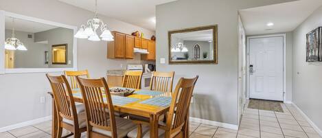 Un comedor con una mesa y sillas de madera, una araña y una cocina al fondo.