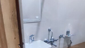 Un baño con lavamanos blanco, un espejo, ducha y un cubo.