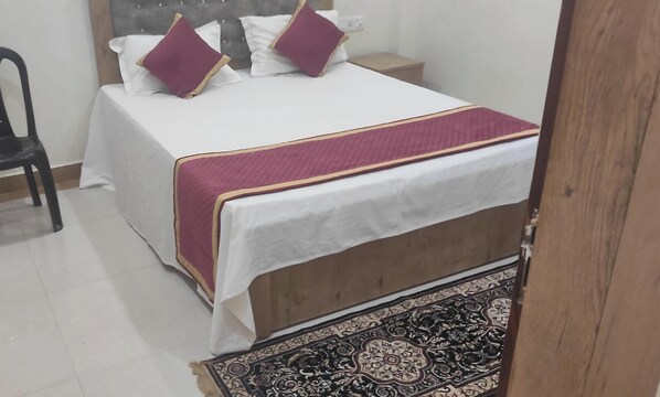 Une chambre à coucher avec un lit, des oreillers, une chaise, une table de chevet et un seau rouge.