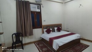 Un dormitorio con una cama individual, una silla, un ventanal con cortinas y un equipo de aire acondicionado.