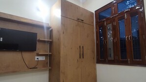 Una habitación con un armario de madera, televisor montado y ventana con marcos de madera.