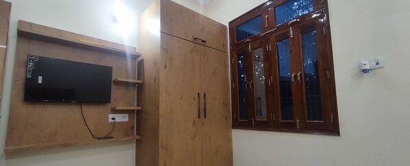 Een kamer met een houten garderobe, een wandtelevisie en een raam met houten kozijnen.