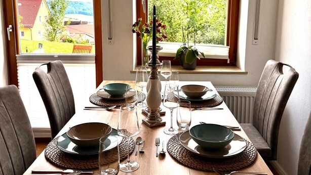 A dining table set for four with a view of a residential area through two windows. - Apartment on the mountain Schloßberg with beautiful view Pet friendly (Heideck)
