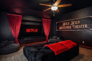 A cozy room with a large TV screen displaying 'NETFLIX', a ceiling fan, and a sign reading 'WILD WILD WESTOVER THEATER'.
