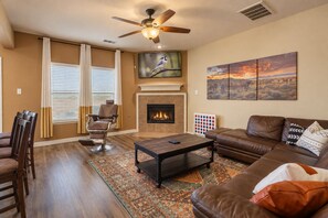 A living room with a fireplace, a ceiling fan, a television, and a large painting on the wall.