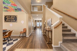 A poker room with a sign, a dining area with chairs, a staircase, and a hallway leading to another room.