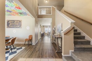 A hallway with a poker-themed wall art, a staircase, and a dining area with chairs and a table.