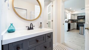 A modern bathroom with a round mirror, a white sink, and dark gray cabinets. - 4-bedroom, 2-bathroom house with pool, hot tub and PS-5 in Clearwater (Clearwater)