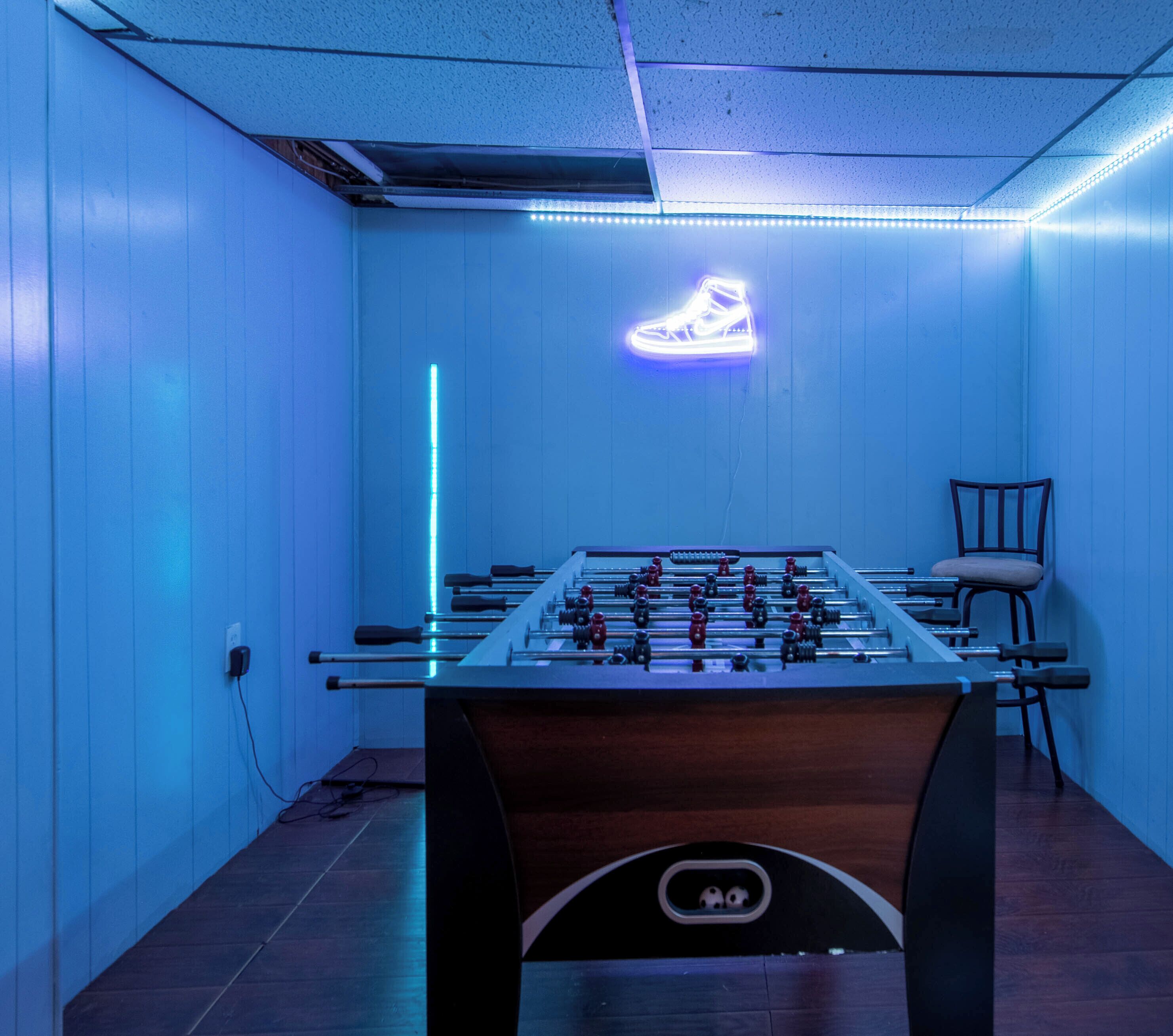 Une pièce avec une table de baby-foot, un panneau lumineux en forme de chaussure et une chaise.
