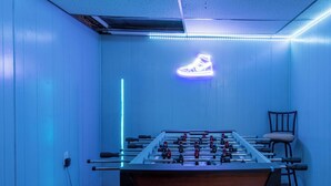 Une pièce avec une table de baby-foot, un panneau lumineux en forme de chaussure et une chaise.