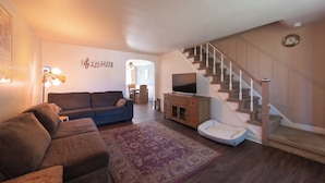 Un salon avec un canapé, un téléviseur, un escalier et un tapis.