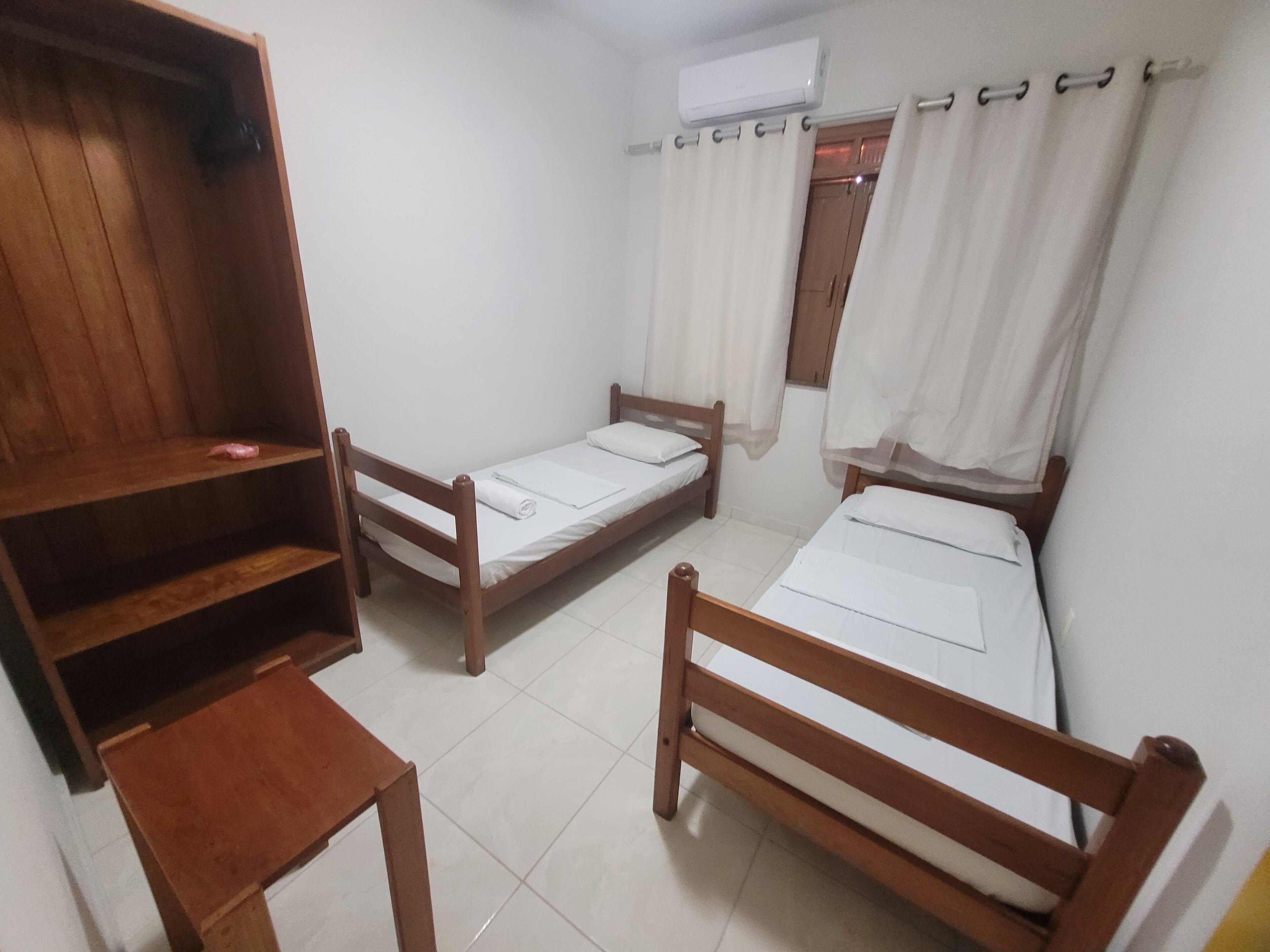 A room with two wooden beds, a wooden table, and a shelf unit.