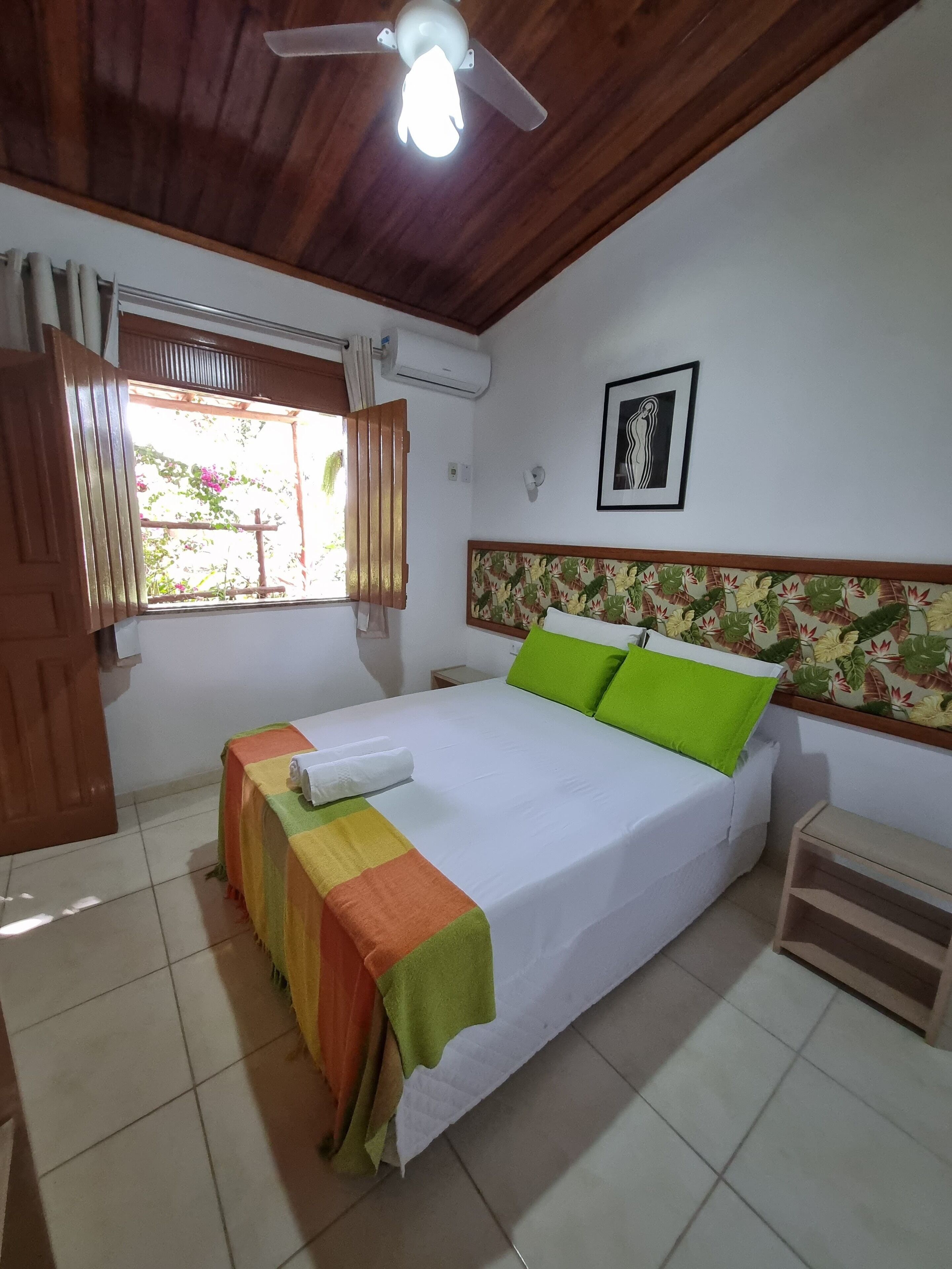 Un dormitorio ordenado con cama, ventana con cortinas, ventilador de techo y aire acondicionado de pared.