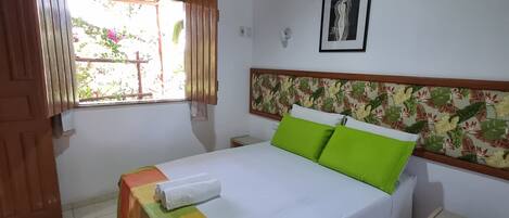 Un dormitorio ordenado con cama, ventana con cortinas, ventilador de techo y aire acondicionado de pared.