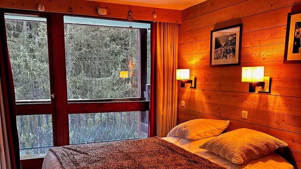 Ein Hotelzimmer mit einem großen Bett, zwei Nachttischlampen, einem mit Vorhängen versehenen Fenster und einem gerahmten Bild an der Wand.
