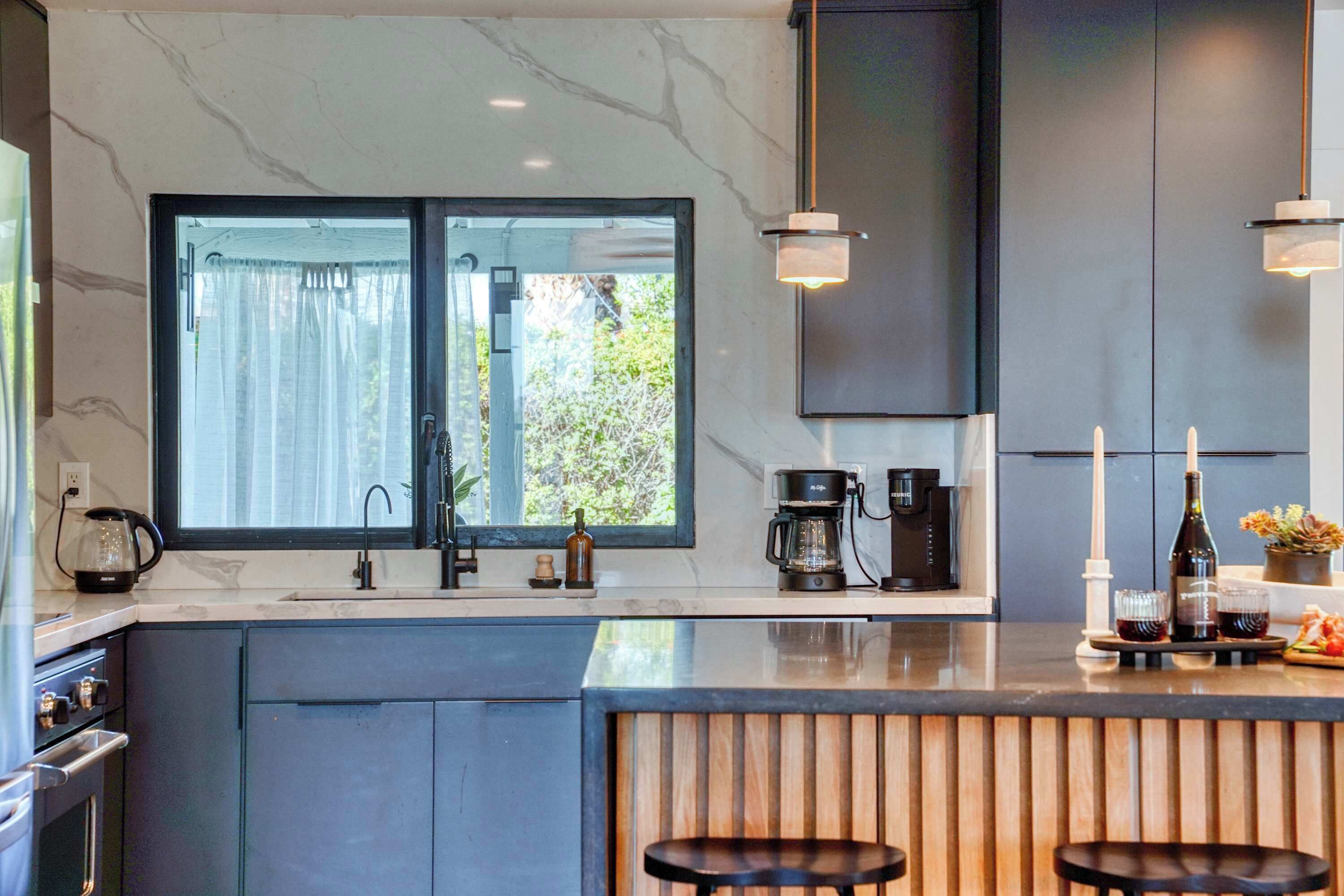 A modern kitchen with a large window, a coffee maker, and a bar area with stools.