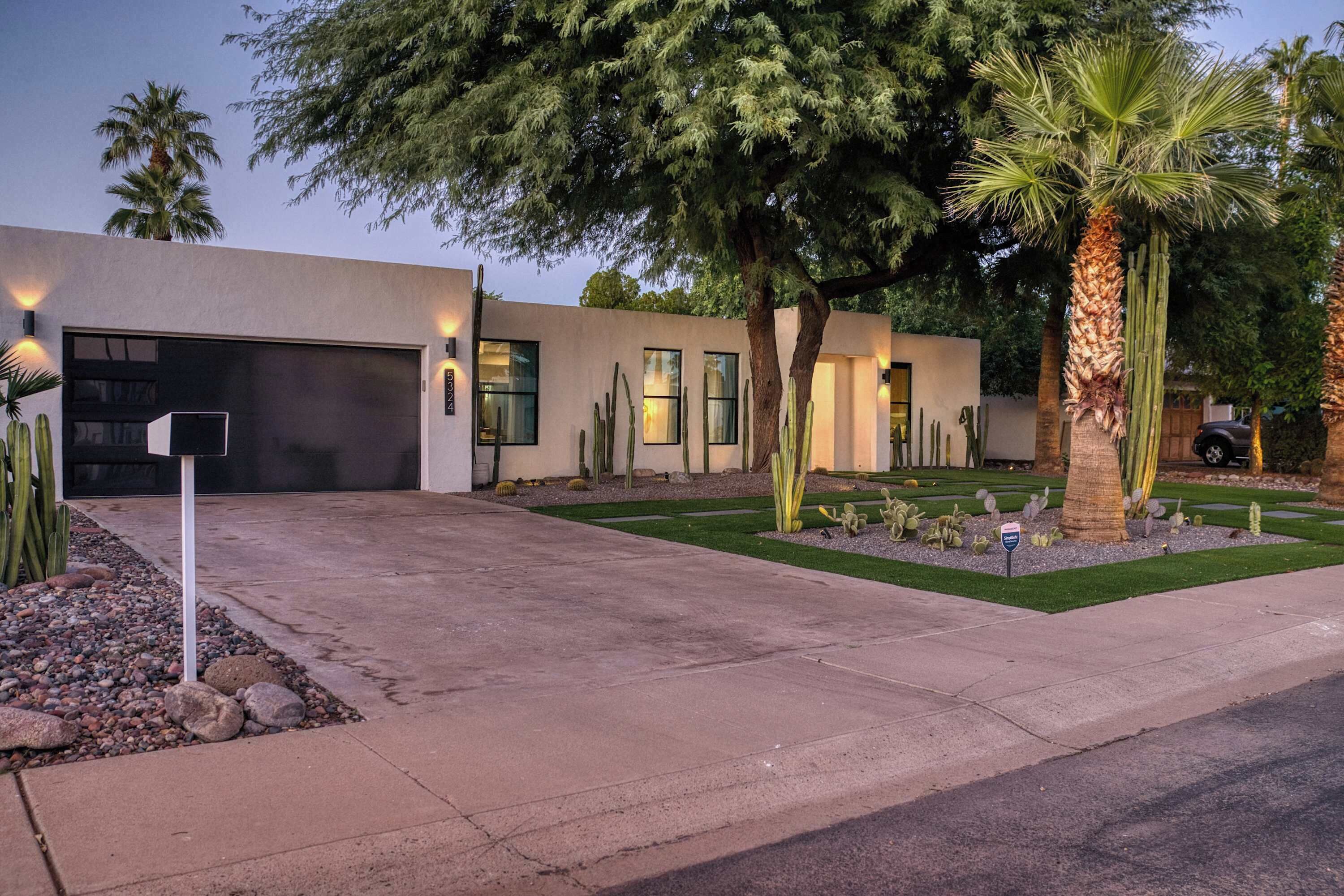 A modern house with a garage, a driveway, and a landscaped garden with cacti and palm trees.