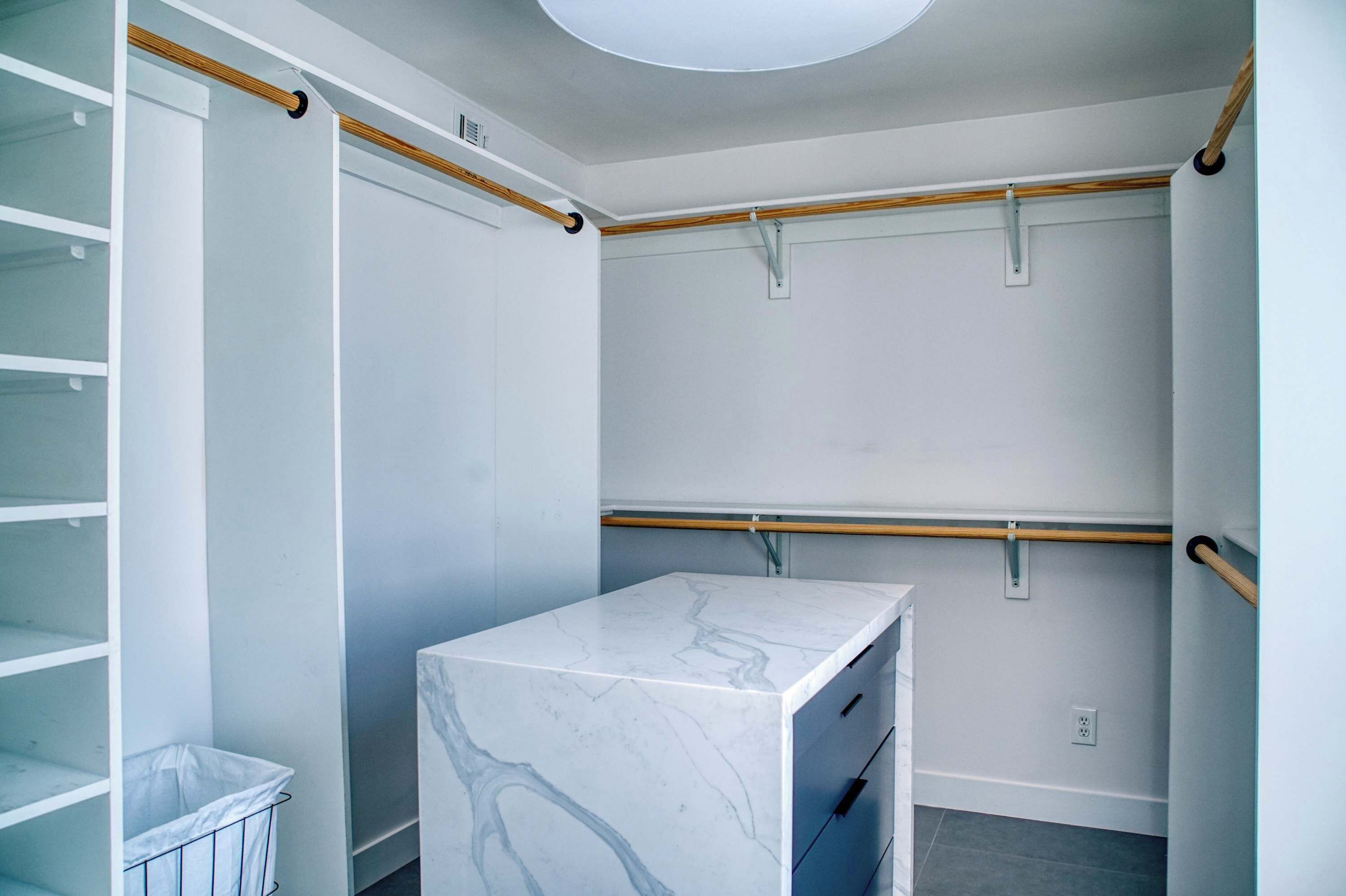 A modern, minimalist walk-in closet with open shelving, a marble vanity, and wooden track lighting.