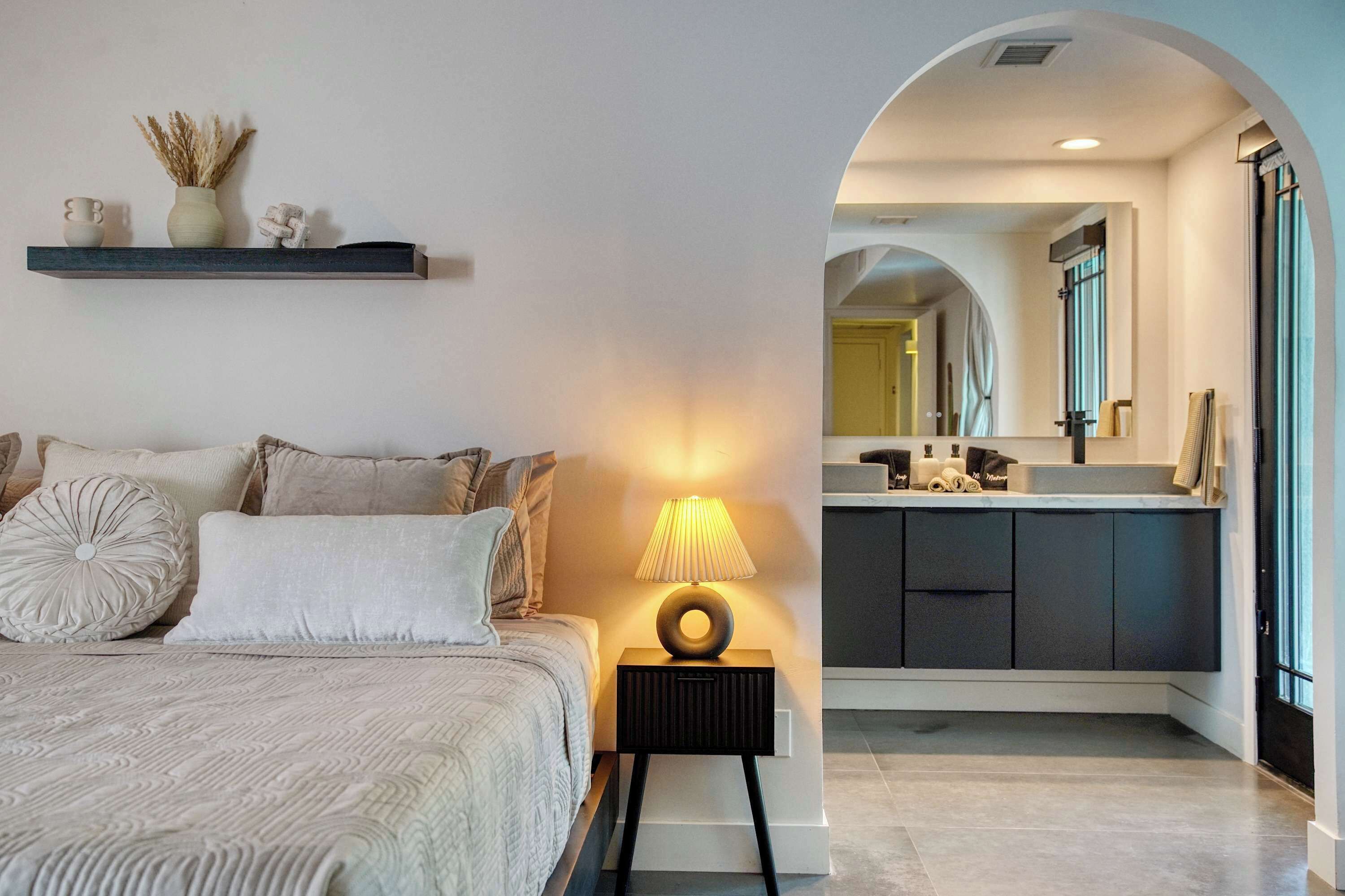 A modern bedroom with a bed, bedside table, and a nightstand with a lamp. There is a built-in bench with storage underneath the bed.