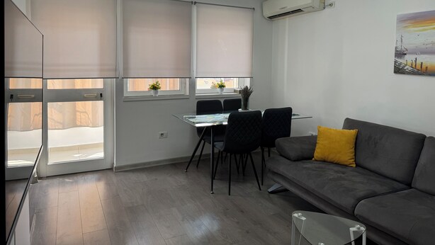 A modern living room with a grey sofa, a dining table with chairs, and a ceiling light fixture. - Tirana Central Square View (Tiranë)