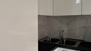 A modern kitchen with white cabinets, a black countertop, and a stainless steel sink. - Tirana Central Square View (Tiranë)