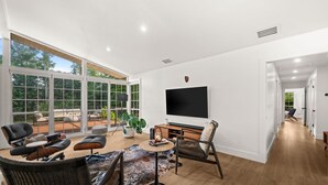 A spacious living area with a large window, a flat-screen TV, and comfortable seating. - Mid-Century Modern · River Walk · Historic McGregor (Fort Myers)