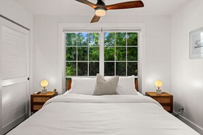 A bedroom with a large window, a ceiling fan, and bedside lamps.