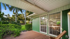 A wooden deck with a chair, a green building with large windows, and lush greenery in the background. - Mid-Century Modern · River Walk · Historic McGregor (Fort Myers)