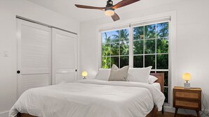 A bedroom with a bed, a ceiling fan, a window with a view of greenery, and a bedside table with a lamp. - Mid-Century Modern · River Walk · Historic McGregor (Fort Myers)