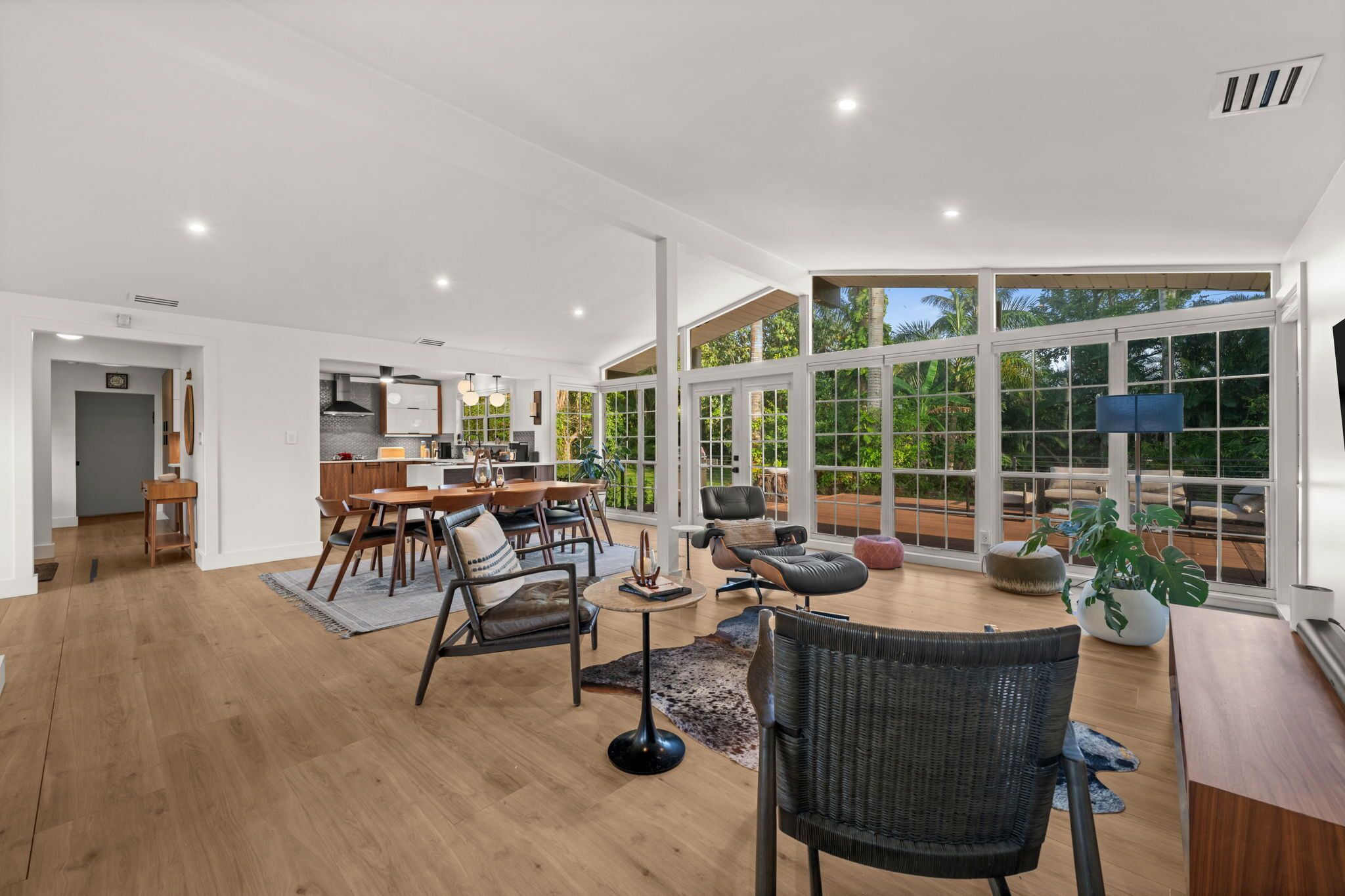 A spacious living area with a dining set, a fireplace, and large windows offering a view of the outdoors.