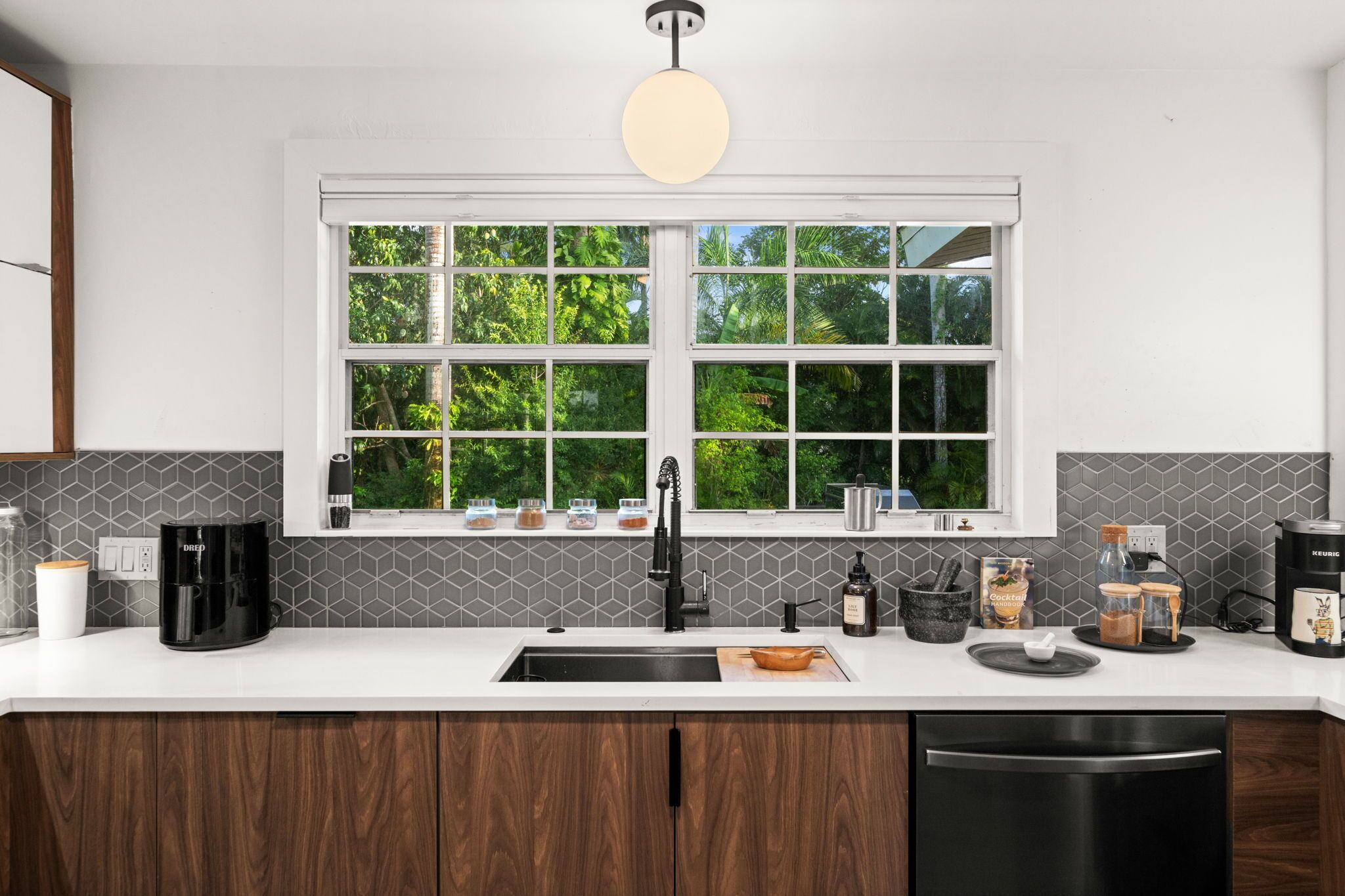 A modern kitchen with a large window, a coffee maker, a kettle, and a coffee machine.