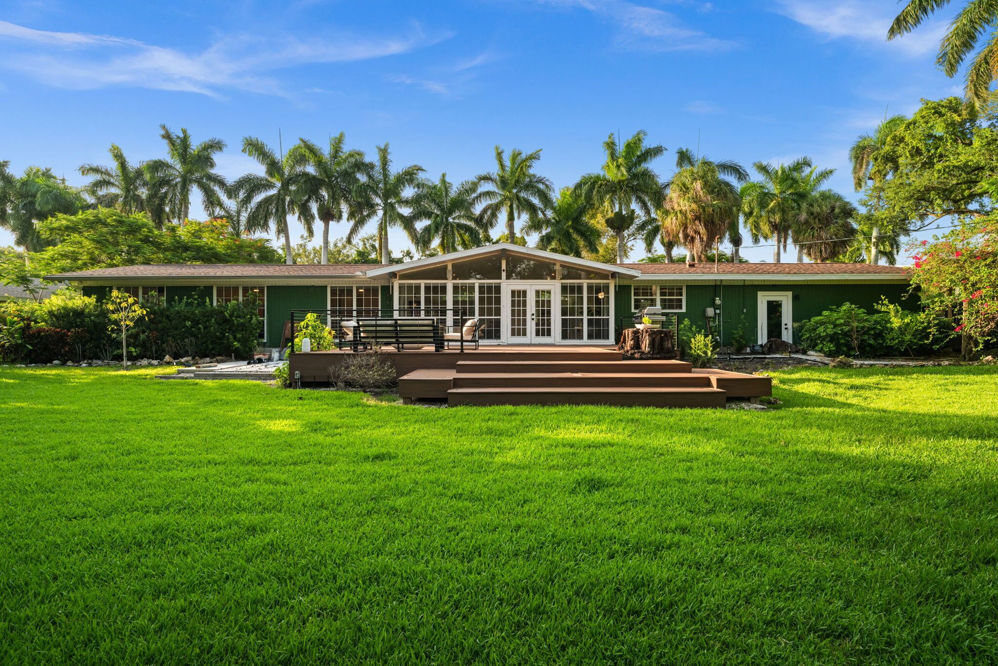 A house with a covered porch, a lawn, and palm trees in the background.
