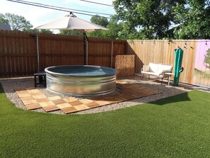 A backyard with a hot tub, a wooden deck, a patio table, and a white outdoor sofa.