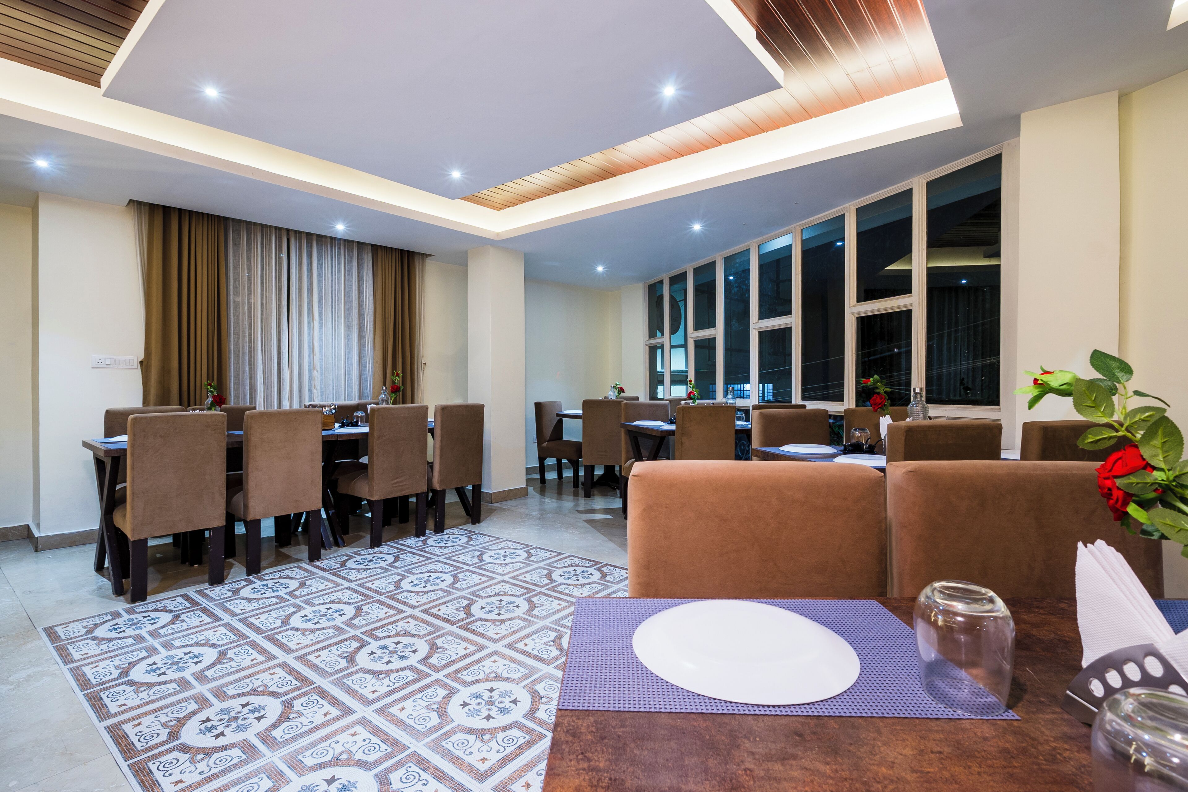 Un espace repas moderne avec un sol à motifs, des chaises recouvertes de tissu marron et une table dressée pour deux personnes.