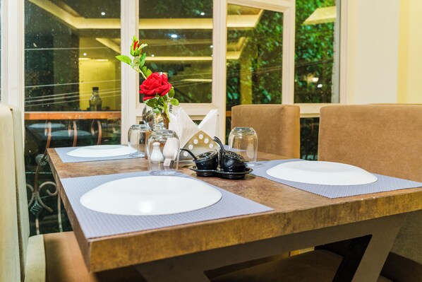 A dining table set with white plates, a vase with a red flower, and a black teapot. - Sucasa Hills Meraki Grand (Gangtok)