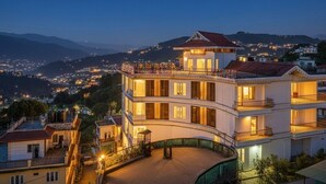 Un edificio de varios pisos con balcones, un patio interior y vistas a un pueblo y montañas al fondo.