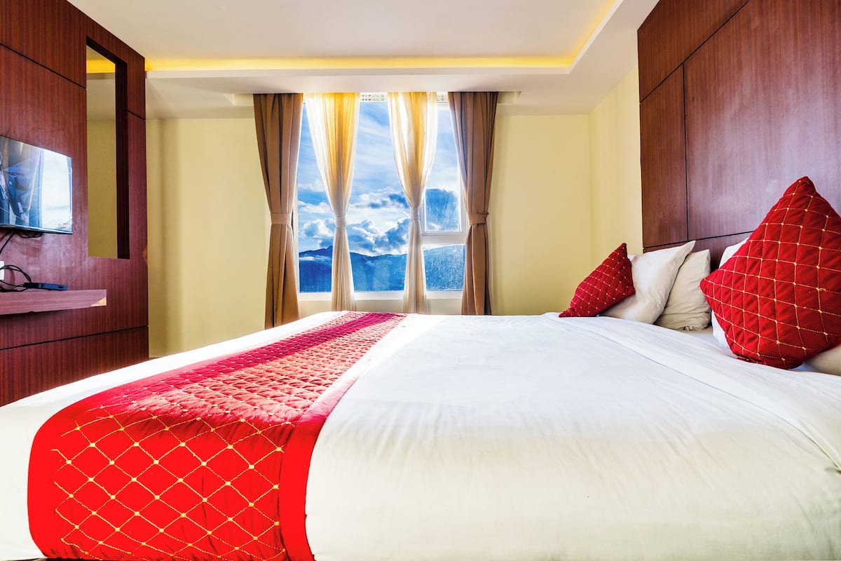 Una habitación de hotel con una cama grande, un televisor sobre un mueble de madera y una ventana con cortinas.