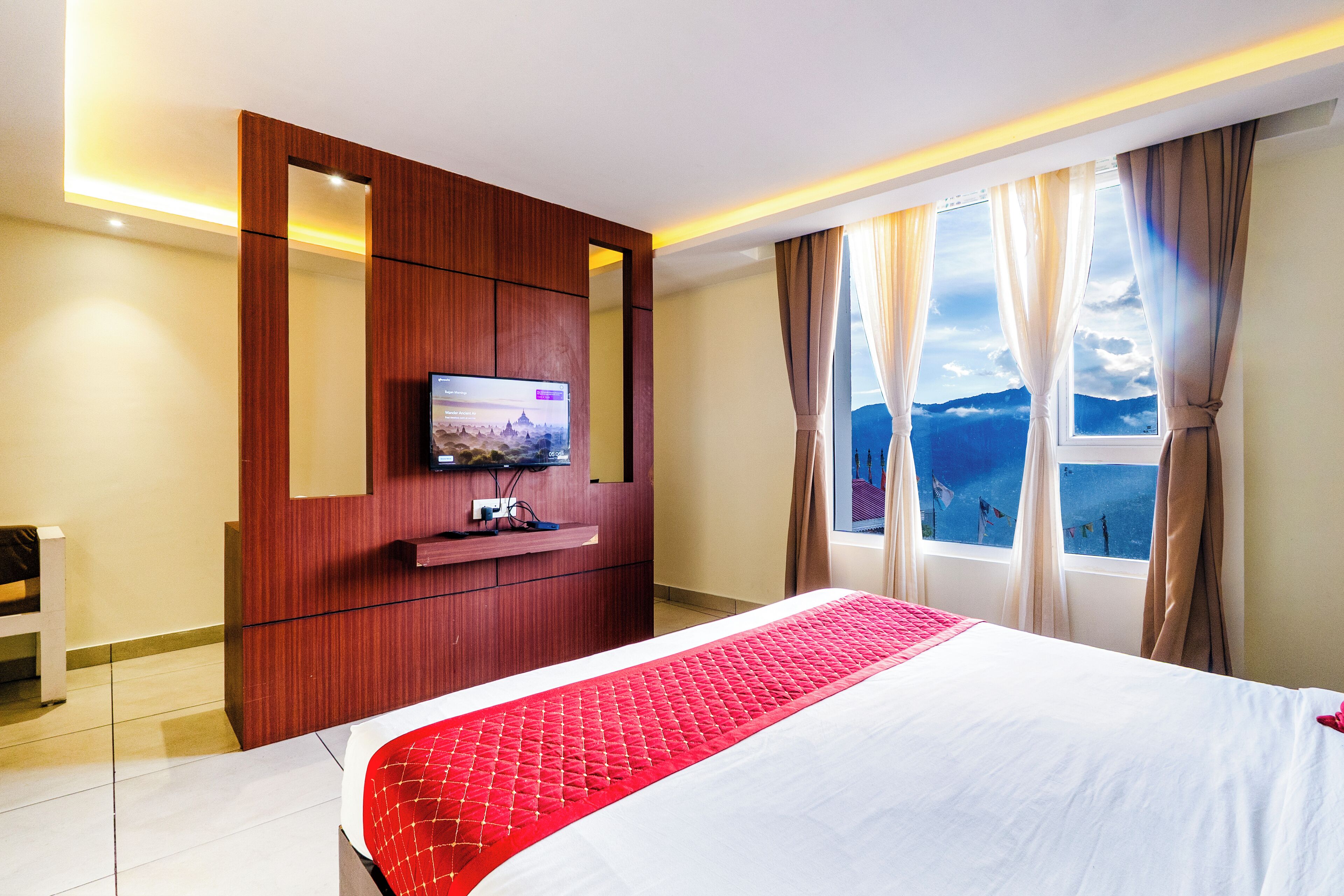 A hotel room with a bed, a TV, a wooden wardrobe, and a window with curtains.