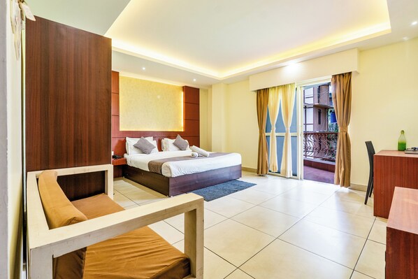 Una habitación de hotel con cama, sofá, escritorio y balcón con cortinas.